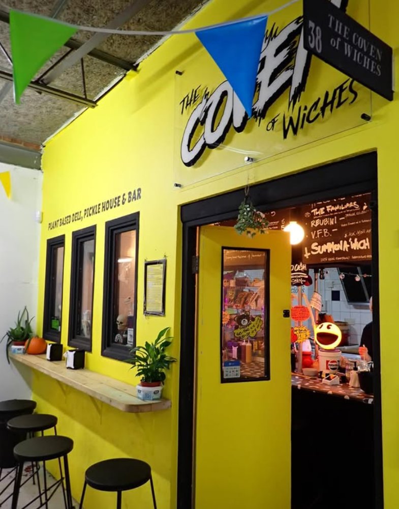 The Coven of Wiches at unit 38, a plant-based deli and pickle house with a bright yellow shopfront and bunting overhead