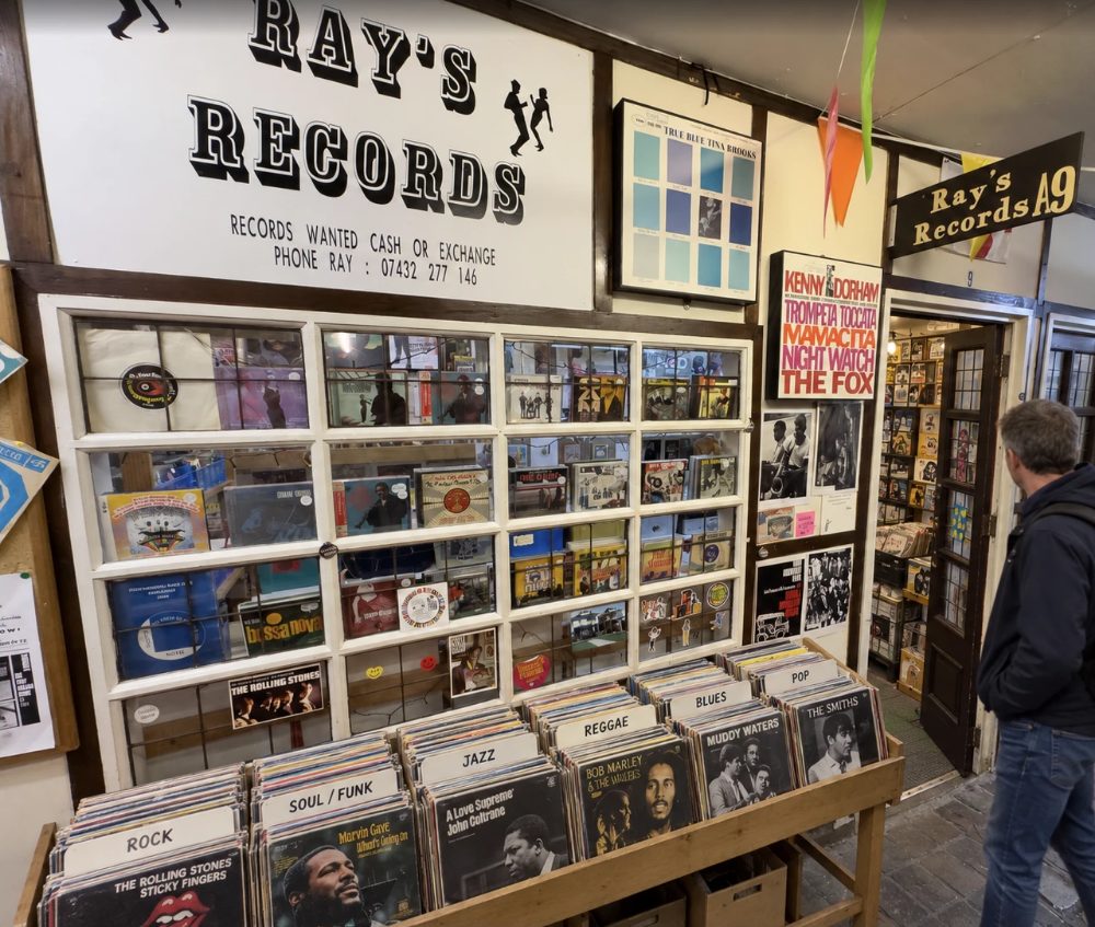 Ray’s Records at unit A9, a wall of album covers under the hand-painted shop sign, with crates of LPs sorted by genre in front